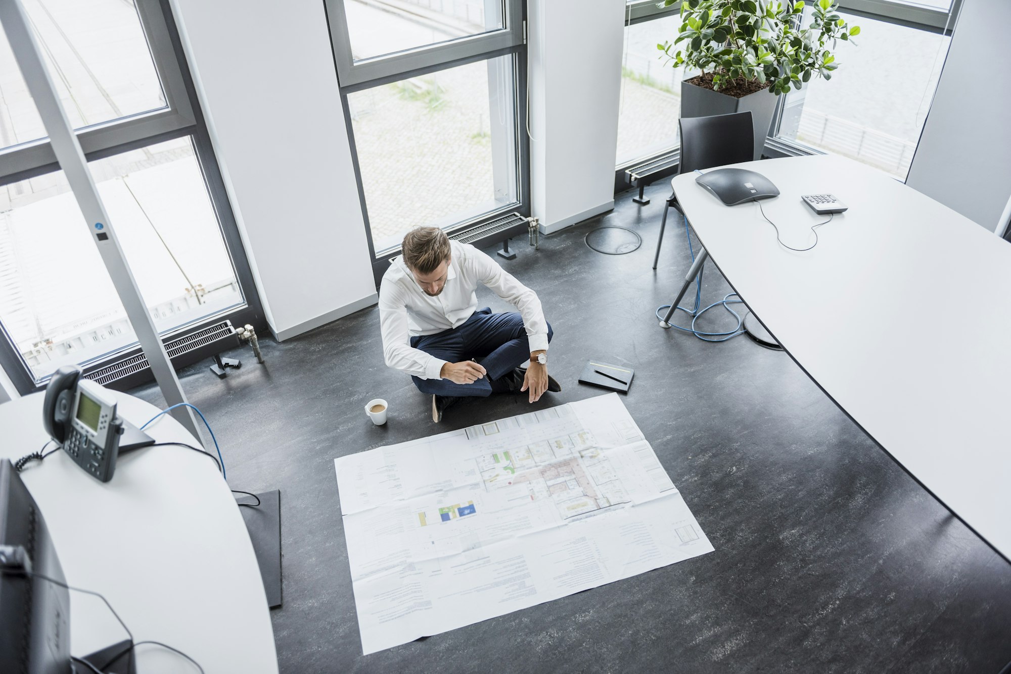 Businessman sitting on the floor of his office looking at construction plan