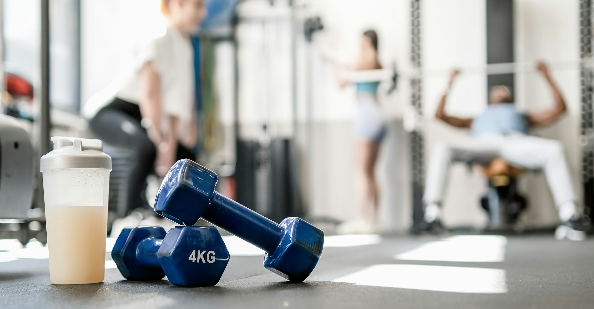 Dumbbells with bottle of protein drink placed on floor in sports club