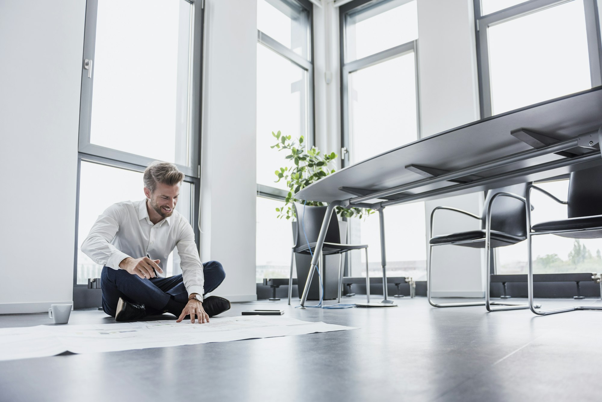 Smiling businessman sitting on the floor of his office looking at construction plan